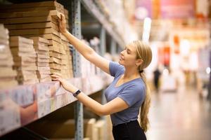 Cheerful woman customer looking up and pulling product on shelf while shopping in hardware store photo