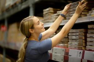 Cheerful woman customer looking up and pulling product on shelf while shopping in hardware store photo