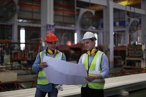 Men industrial engineer wearing a safety helmet while standing in a heavy industrial factory. The Maintenance looking of working at industrial machinery and check security system setup in factory. photo