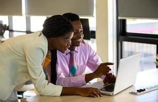 Diverse business colleagues sitting at a desk in a modern office talking together over a laptop photo