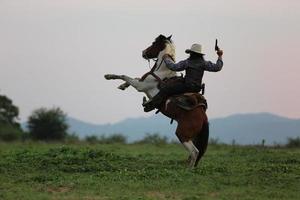 vaquero montando a caballo con la mano sosteniendo un arma contra el fondo del atardecer.
