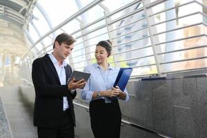 hombre de negocios que muestra contenido en tableta a una colega. hombre y mujer de negocios caminando afuera, usando tableta, hablando, sonriendo, riendo. concepto de comunicación foto