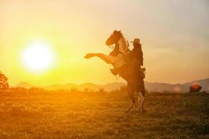 vaquero a caballo contra una hermosa puesta de sol, vaquero y caballo a primera luz, montaña, río y estilo de vida con fondo de luz natural foto