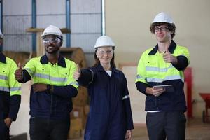 Tres ingenieros y trabajadores multiculturales de la industria pesada uniformados revisan el brazo robótico automático para usar en la fábrica. la contratista industrial femenina está usando una tableta. foto