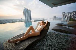 Young woman enjoying and relaxing at poolside. Slim young girl model in white bikini  by the pool. photo