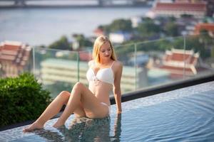 mujer joven disfrutando de un sol, modelo de niña delgada en bikini blanco junto a la piscina.