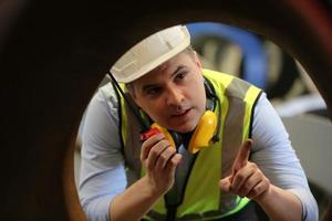 ingeniero industrial masculino con casco de seguridad mientras está de pie en una fábrica industrial pesada. el mantenimiento que busca trabajar en maquinaria industrial y verificar la configuración del sistema de seguridad en fábrica. foto