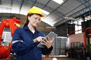 Professional young industrial factory woman employee working with machine part, checking and testing industrial equipment and robot arms in large Electric electronics wire and manufacturing plant photo