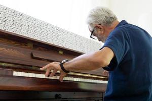 Retired elderly man with gray hair are playing piano on daytime for relaxing photo