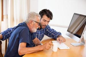 adult man teaching elderly man to using computer at home. photo