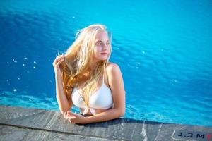 mujer joven disfrutando y relajándose junto a la piscina. modelo de chica joven delgada en bikini blanco junto a la piscina. foto