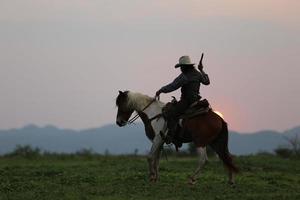 Cowboy riding horse with hand holding gun against sunset background. photo