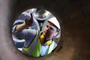 ingeniero industrial masculino con casco de seguridad mientras está de pie en una fábrica industrial pesada. el mantenimiento que busca trabajar en maquinaria industrial y verificar la configuración del sistema de seguridad en fábrica. foto