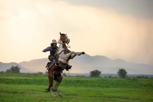 Cowboy riding horse with hand holding gun against sunset background. photo