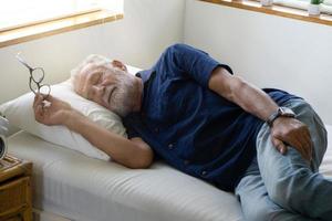 Retried elderly man with gray hair are sleeping on bedroom on daytime for relaxing. photo