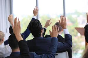 business people in seminar raising hand for vote at meeting activity or business event asking question at speaker's seminar or workshop