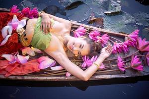 jóvenes asiáticas con vestimenta tradicional en el bote y flores de loto rosa en el estanque.hermosas chicas con traje tradicional.chica tailandesa con vestido retro tailandés, chica tailandesa con traje tradicional foto