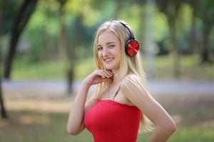 Beautiful blonde woman standing while listening music on headphone at park.