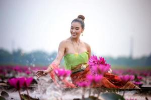 jóvenes asiáticas con vestimenta tradicional en el bote y flores de loto rosa en el estanque.hermosas chicas con traje tradicional.chica tailandesa con vestido retro tailandés, chica tailandesa con traje tradicional foto