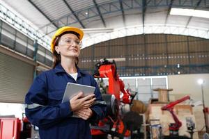 Professional young industrial factory woman employee working with machine part, checking and testing industrial equipment and robot arms in large Electric electronics wire and manufacturing plant photo