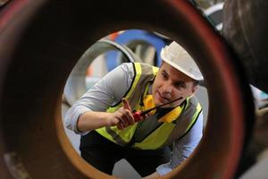 ingeniero industrial masculino con casco de seguridad mientras está de pie en una fábrica industrial pesada. el mantenimiento que busca trabajar en maquinaria industrial y verificar la configuración del sistema de seguridad en fábrica. foto