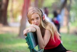 hermosa mujer rubia de pie mientras escucha música en los auriculares en el parque.