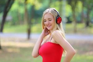 Beautiful blonde woman standing while listening music on headphone at park. photo