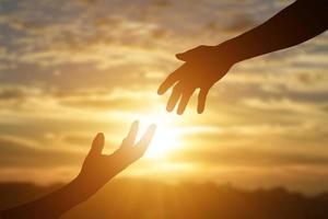 silueta de dar una mano amiga, esperanza y apoyo mutuo sobre el fondo de la puesta de sol.