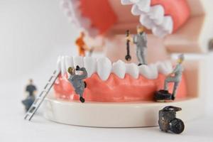 miniature people to repair a tooth or small figure worker cleaning tooth model as medical and healthcare. photo