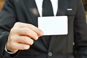 Closeup of businessman showing white piece of paper in black suit. Idea for business credit card or visiting card. photo