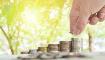 Businessman hand putting coins stack on table with blur nature bokeh background in park. Concept financial saving success growing investment. photo