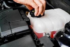 el mecánico inspecciona el tanque de expansión con anticongelante rosa. nivel de refrigerante del vehículo en el sistema del radiador del automóvil. autopartes foto