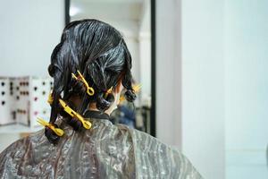 una joven asiática tiene un corte de pelo y un spa con un peluquero de belleza profesional. mujer sentada en la silla de belleza - salón de belleza mientras el peluquero le corta el pelo. foto