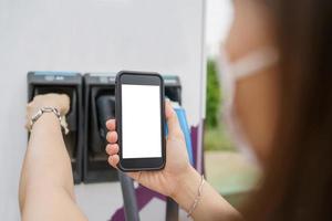 pantalla vacía del teléfono inteligente de maqueta aislado con ruta de recorte. mujer joven asiática que usa la aplicación de carga ev en el teléfono inteligente se conecta con la estación de carga, bev o estación de carga de vehículos eléctricos foto