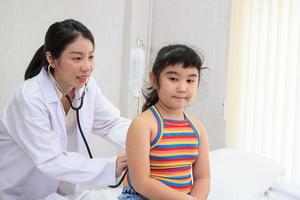 médico especialista profesional que examina la respiración de una niña asiática en un hospital infantil. doctor amablemente revisando y escuchando los latidos del corazón en una niña. foto