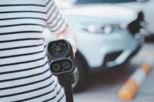 mujer joven asiática preparándose para cargar su vehículo eléctrico o auto ev en la estación de carga ev. foto