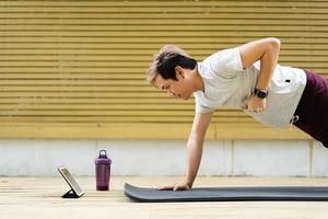 deportista activo haciendo un ejercicio de tabla lateral y haciendo una videollamada con un amigo y entrenador de entrenamiento deportivo en línea. hombre deportivo saludable haciendo un entrenamiento de culturismo con un instructor en línea. foto