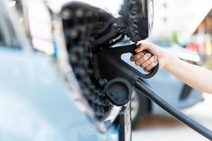 mujer joven asiática preparándose para cargar su vehículo eléctrico o auto ev en la estación de carga ev. foto