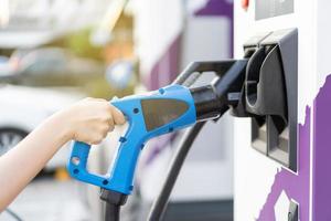 mujer joven asiática preparándose para cargar su vehículo eléctrico o auto ev en la estación de carga ev. foto