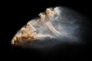 explosión de arena aislada sobre fondo negro. congelar el movimiento de las salpicaduras de polvo arenoso. foto