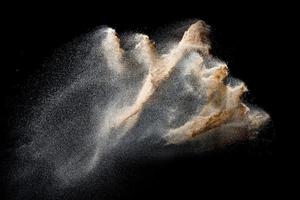 Sand flying explosion isolated on black background. Freeze motion of sandy dust splash. photo