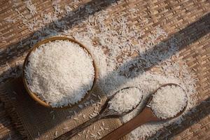 Sunlight and shadow on surface of white rice in ceramic bowl with wooden spoons on threshing basket, top view with copy space photo