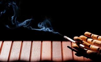 Wooden mannequin hand holding cigarette on wood plank floor in dark background photo