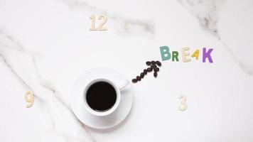 Top view of black coffee in white ceramic cup and coffee bean line in clock hand shaped with wooden numbers and Break word in clock face forming on white marble tabletop, coffee break time concept photo