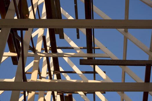 Sunlight and shadow on surface of the old wooden roof structure in incomplete house building site against blue sky in evening time, low angle view and selective focus photo