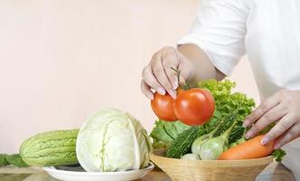 Overweight woman's hand preparing various fresh vegetables into bamboo basket for cooking in kitchen area photo