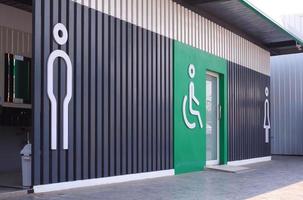 Side view and focus on foreground of male, disabled wheelchair and female signs on wood panel and green wall decorations of public restroom