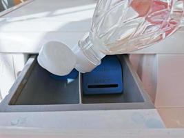 Close up hand pouring the vinegar into the front-loading drawer. Clean a washing machine with vinegar. photo