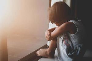 una niña asiática triste estaba llorando y sentada en el suelo cerca de la puerta de la habitación. ella fue intimidada, infeliz, molesta, se siente enferma. concepto solitario. foto