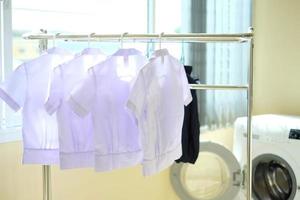 Student uniforms after washing hang on the clothes line. White shirts and blue skirts drying on clothes rack inside the house. Back to school concept. photo